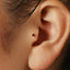 A close-up of a person's ear with a small red gemstone inserted in the earlobe.
