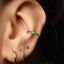 A close-up view of a person's ear adorned with a green gemstone earring and a silver earring.