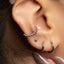 A close-up view of a person's ear adorned with multiple silver hoop earrings, including a hoop earring with a small ball at the bottom and a hoop earring with a small ball at the top.