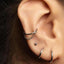 A close-up view of a person's ear adorned with multiple silver earrings, including a hoop earring, a chain earring, and a small earring.