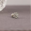 A silver-toned flower-shaped earring with a small center stone is displayed on a gray fabric surface.