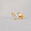A gold-colored earring with a clear gemstone in the shape of a heart, resting on a white surface.
