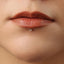 A close-up of a person's lips with a small diamond-like object inserted in the lower lip area.