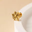 A gold-colored earring in the shape of a spider web is resting on a white surface.