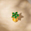 A gold-colored earring with a flower-like design and green gemstones is shown against a glittery background.