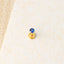A gold-colored earring with a blue gemstone is placed on a white surface.