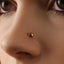 A close-up of a person's nose and eye, with a small gold-colored nose ring featuring a fish-shaped design.
