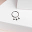 A silver ring with three small star-shaped charms hanging from it, placed on a white surface.