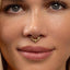 A close-up of a woman's face, focusing on her nose and lips. She is wearing a gold nose ring with a floral design.