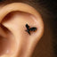 A person's ear with a small black bat-shaped earring inserted in the earlobe.