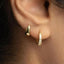 A close-up view of a person's ear, showing two gold earrings with small diamonds.