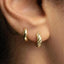 A close-up view of a person's ear, showing two gold hoop earrings.