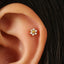 A small gold-colored earring with a flower-shaped design and small diamonds is visible in the image.