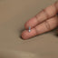 A person's hand holding a small silver flower-shaped charm on the index finger.