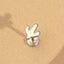 A small silver earring with a unique design is shown against a textured beige background.