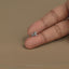 A person's thumb is holding a small silver charm in the shape of a dog.