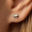 A close-up view of a person's ear, showing a small silver earring in the shape of a fish.
