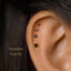 a close-up of a person's ear with several small black gemstone studs, likely earrings, inserted into the earlobe.