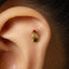 A gold earring with a red gemstone is visible in the person's ear.