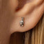 A small silver earring with a hand gesture on it is visible in the image.