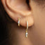 A close-up view of a person's ear adorned with two gold earrings, one of which is a drop earring with a clear gemstone dangling from it.