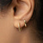 A close-up view of a person's ear with two gold hoop earrings attached.