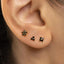 A close-up view of a person's ear adorned with three small, black diamond-shaped earrings.