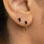 A close-up of a person's ear with two small gold earrings, one with a rectangular gemstone and the other with a pointed gold accent.