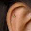 A small gold-colored earring with a green gemstone is visible in the image.