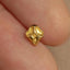 A close-up image of a person's fingers holding a small, intricately designed gold-colored object, which appears to be a small, gold-colored gemstone or a small gold-colored piece of jewelry.