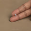 A person's left hand is holding a small silver object, which appears to be a tiny piece of jewelry or a small decorative item.