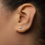 A close-up of a person's ear with a small silver triangle-shaped earring in the earlobe.