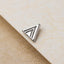 A silver triangular earring is resting on a textured surface.