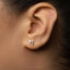 A close-up of a person's ear with a small silver earring featuring a Hebrew letter, likely the letter "S" or "S," attached to it.