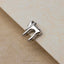 A silver-colored metal charm or pendant is resting on a textured surface, such as a piece of paper or a fabric.