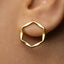 A close-up view of a person's ear wearing a gold-colored geometric earring.