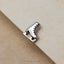 A silver metal ice skating shoe charm is placed on a textured surface.