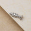 A silver-colored metal object resembling a small musical instrument, such as a flute or clarinet, is placed on a textured surface.