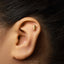 A gold earring with a small coffee cup design is visible in the person's ear.