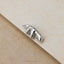 A small silver metal object resembling a cat or feline is resting on a textured surface.