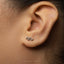 A close-up view of a person's ear with a small silver earring featuring a snake-like design.