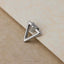 A silver triangular earring with a pointed end rests on a textured surface.