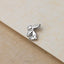 A small silver rabbit ear earring is resting on a textured surface.