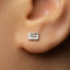 A close-up of a person's ear with a small, square-shaped earring in the earlobe.