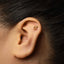 a close-up view of a person's ear with a gold-colored male symbol piercing in the earlobe.