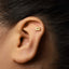 A gold earring with a small cassette tape design is visible in the person's ear.