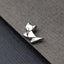 A silver metal cat-shaped object is resting on a textured gray surface.