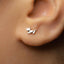 A close-up view of a person's ear adorned with a small silver earring featuring a leaf-like design.