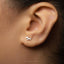 A close-up view of a person's ear adorned with a small silver earring featuring a leaf-like design.