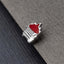 A small, silver-colored pin with a red, flame-like design on it, resting on a gray surface.